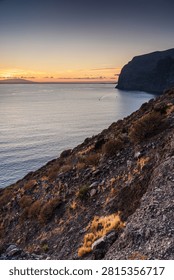 The sun sets behind the imposing cliffs of Los Gigantes, casting a warm glow over the Atlantic Ocean waters