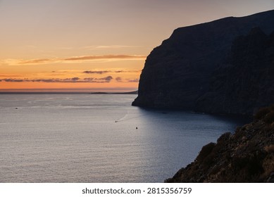 The sun sets behind the imposing cliffs of Los Gigantes, casting a warm glow over the Atlantic Ocean waters