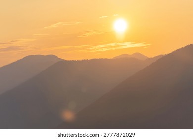 The sun sets behind the mountains, casting warm light across the peaks. The sky shows hints of color as day turns into night. The scene captures the beauty of nature at dusk.