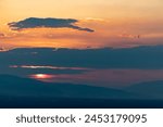 The sun sets behind mountains in Pamukkale, casting a warm orange glow across the layered clouds.