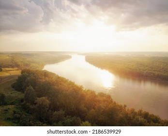 The sun sets behind the river and fills the trees with warm evening light, fog rises in the rays of golden light. Clouds and clouds are reflected in the water. river Ob. - Shutterstock ID 2186539929