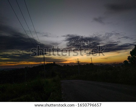 the sun sets between a hill and an electric cable pole