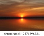 The sun sets beyond the horizon, casting a soft golden glow reflected on the calm water. Silhouettes of trees and the serene atmosphere add depth and a dreamy, captivating charm to the scene.