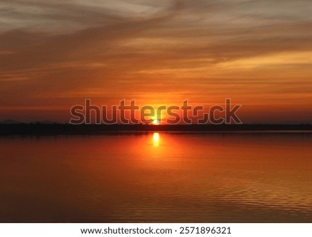 The sun sets beyond the horizon, casting a soft golden glow reflected on the calm water. Silhouettes of trees and the serene atmosphere add depth and a dreamy, captivating charm to the scene.