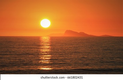 The sun sets into a ocean background with dolphins splashing in the foreground.