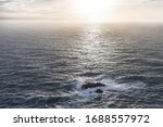 the sun sets into the ocean. Waves breaking on rocks