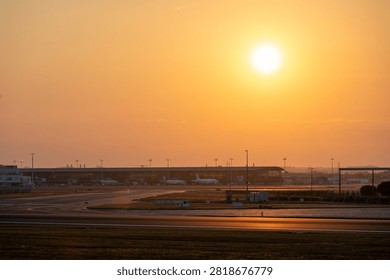 The sun sets low over the runway and open ground at Brussels Airport in Belgium, a calm and glowing evening scene at the airfield.