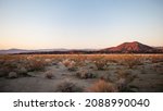 The sun sets on a hill in the distance with a foreground of sage brush in the Mojave Desert