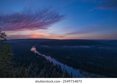 As the sun sets on the horizon, vibrant hues fill the sky above a peaceful river winding through a dense forest, creating a serene evening atmosphere. - Powered by Shutterstock