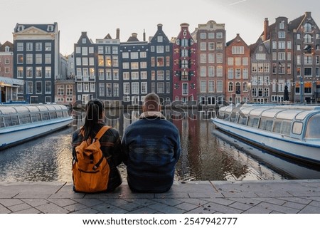 As the sun sets over the iconic canals of Amsterdam, a couple sits peacefully, surrounded by colorful Dutch architecture and the vibrant hues of autumn foliage, creating a serene escape.