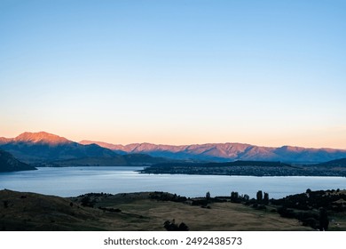 The sun sets over a mountain lake, casting a warm glow over the serene landscape and creating a peaceful, picturesque scene.