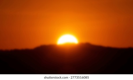 The sun sets over a mountain range, creating a beautiful silhouette against the orange sky. The image captures the beauty of nature and the peacefulness of the evening.