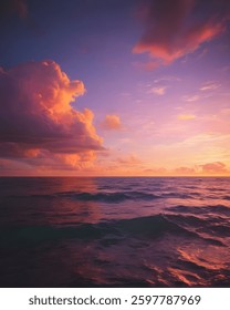 The sun sets over the ocean, casting brilliant orange and pink clouds that mirror on the calm water, creating a harmonious composition.
