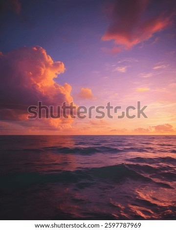 The sun sets over the ocean, casting brilliant orange and pink clouds that mirror on the calm water, creating a harmonious composition.