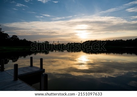 the sun sets over a pier and a lake one summer evening