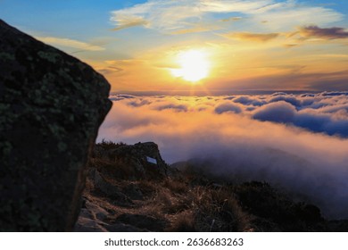 The sun sets over a rolling cloudscape viewed from a rocky outcrop in the Victorian Alps, Australia on August 31, 2011, combining rugged terrain and peaceful sky.
