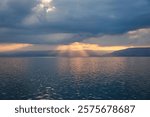 The sun sets over the Sea with dramatic clouds and sunlight breaking through, creating a serene and beautiful scene.