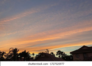 The Sun Sets Over A South Florida Neighborhood Lined With Palm Trees. The Stratocomulus Clouds Turn A Burnt Orange As The Sun Goes Down. 