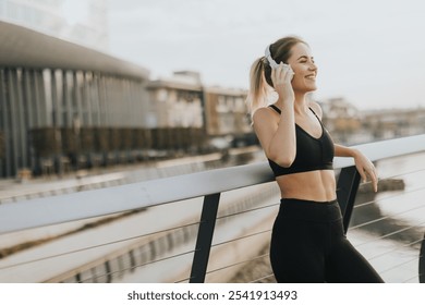 As the sun sets over the water, a young woman leans against a railing, savoring her favorite tunes through headphones, embracing tranquility and peace. - Powered by Shutterstock