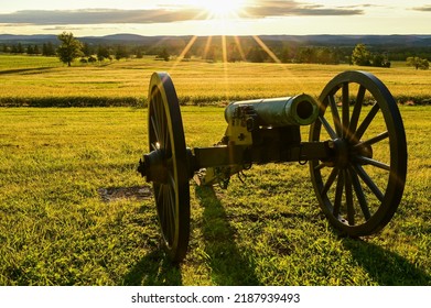 Sun setting behind a cannon pointed over a field