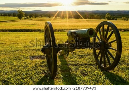 Sun setting behind a cannon pointed over a field