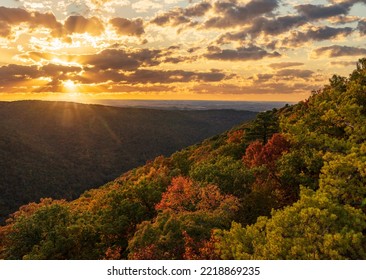 Sun setting behind clouds illuminating the fall colors of the trees in Coopers Rock State Forest