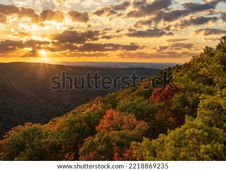 Sun setting behind clouds illuminating the fall colors of the trees in Coopers Rock State Forest