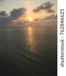 Sun setting behind clouds over the calm lagoon waters of Isla Blanca, golden light reflecting across the surface toward a quiet beach, Cancun, Mexico