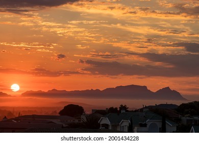 The Sun Is Setting Behind Fish Hoek Accross False Bay. The Back Of Table Mountain And Devils Peak Are Visible