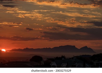The Sun Is Setting Behind Fish Hoek Accross False Bay. The Back Of Table Mountain And Devils Peak Are Visible