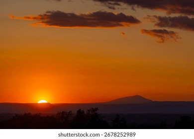 Sun setting behind horizon casting warm glow across sky and silhouetting distant mountain range