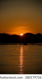 Sun setting behind a mountain peak over the river water