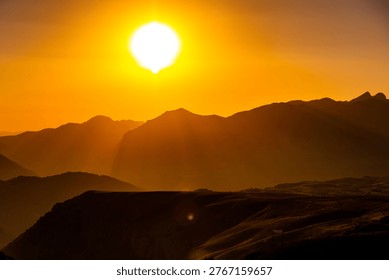 Sun setting behind a mountain range, creating dramatic silhouettes and warm golden light across the landscape