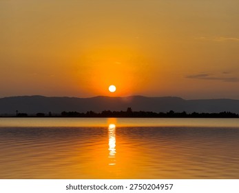 The sun is setting behind the mountains, and its light is reflected on the water's surface.