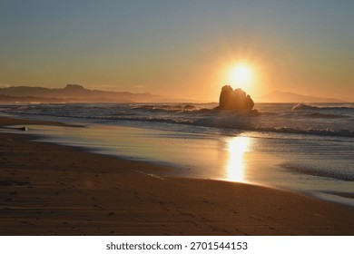Sun setting behind a rock formation on Ilbarritz beach between Biarritz and Bidart