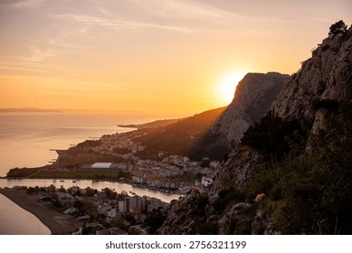 Sun setting behind the rugged mountains of Omiš, casting a warm light over the town where the Cetina river meets the Adriatic Sea, highlighting the dramatic coastal landscape