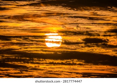The sun is setting behind a thick layer of textured clouds, creating a vibrant display of orange and yellow hues across the sky