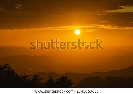 Sun setting, casting a warm orange glow over rolling mountains and distant trees