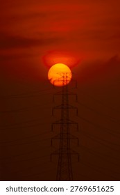 The sun setting directly behind the top of an electricity tower, creating an intense orange glow and industrial silhouette.