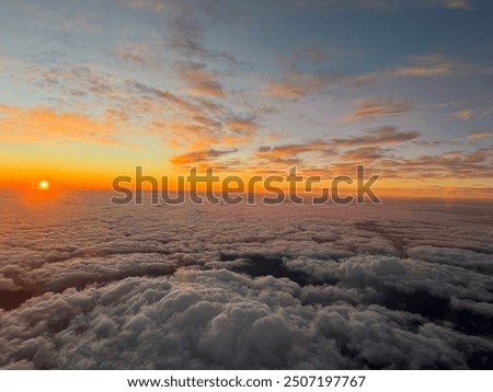 The sun setting into the clouds. Image courtesy of out of the airplane window during sunset in Kauai Hawaii USA