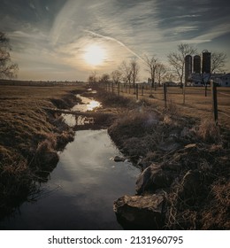 The Sun Is Setting Just Above A Small And Humble Stream Passing Through Lancaster, Pennsylvania Amish Country.