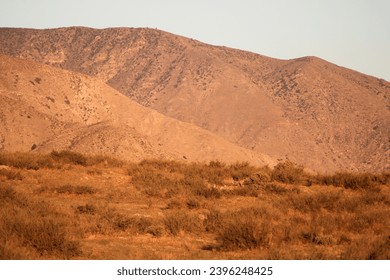 Sun setting on an arid desert plain with barren mountains beyond taken at an arid field in Cabazon, CA