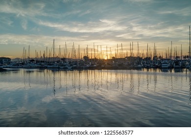 Sun setting on Emeryville Marina. Sailboats moored in San Francisco Bay with sunset skies and water reflections. Alameda County, California, USA.