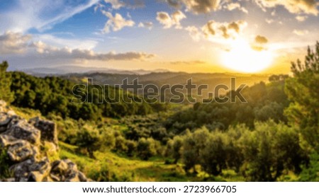 Sun setting over green rolling hills with trees and blue skies filled with white clouds.