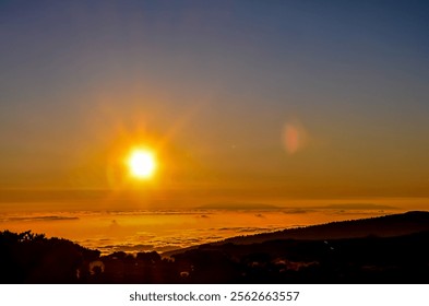 The sun is setting over a mountain range, casting a warm glow over the landscape. The sky is a deep blue, with a few clouds scattered throughout. The scene is peaceful and serene