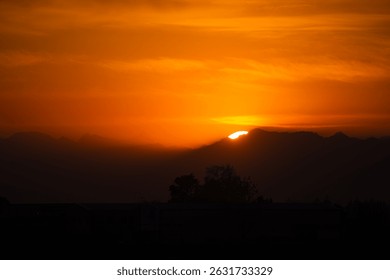 Sun Setting Over Mountain Range with Vivid Orange Sky and Shadows