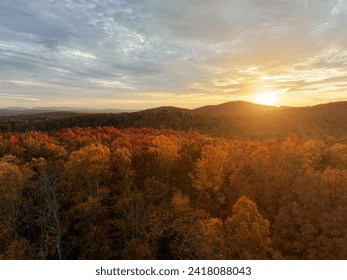 Sun setting over mountains with rays of sunlight shining on deciduous trees showing fall colors. 