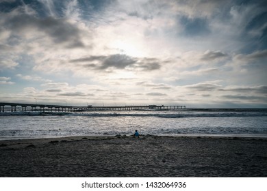 The sun setting over Ocean Beach pier as a child plays in the middle of the sand near the water under the setting sun. 