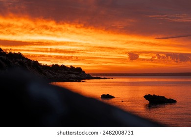 The Sun setting over ocean beach with rocks in water