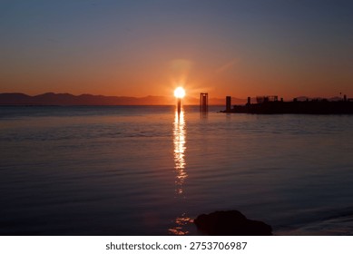 a sun setting over the ocean behind the mountains and the reflection of the sun dances on the water 